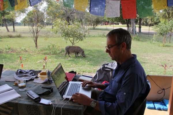 Professor David Bunn assessing data from the field house in Kruger National Park in South Africa where he and Melissa McHale lived. A bored warthog grazes nearby.