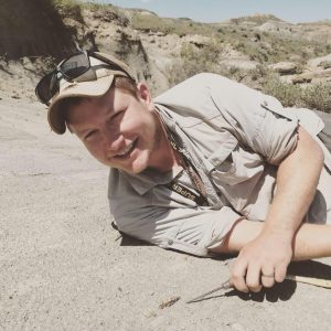 Luke Weaver leaning on ground in badlands in front of a Oxyprimus fossil jaw
