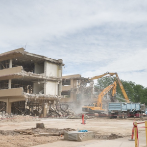 Construction workers spraying water on demolished building and debris piles.