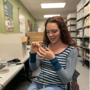 Student examines a stone artifact inside a lab space with bookshelves behind