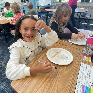 Elementary school student holds a replica projectile point in front of a plate of sand