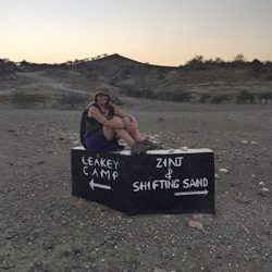 Anthropology student sitting on a sign for photo