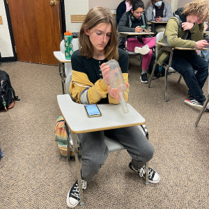 Student seated looking at a glass bottle from a historical archaeological site