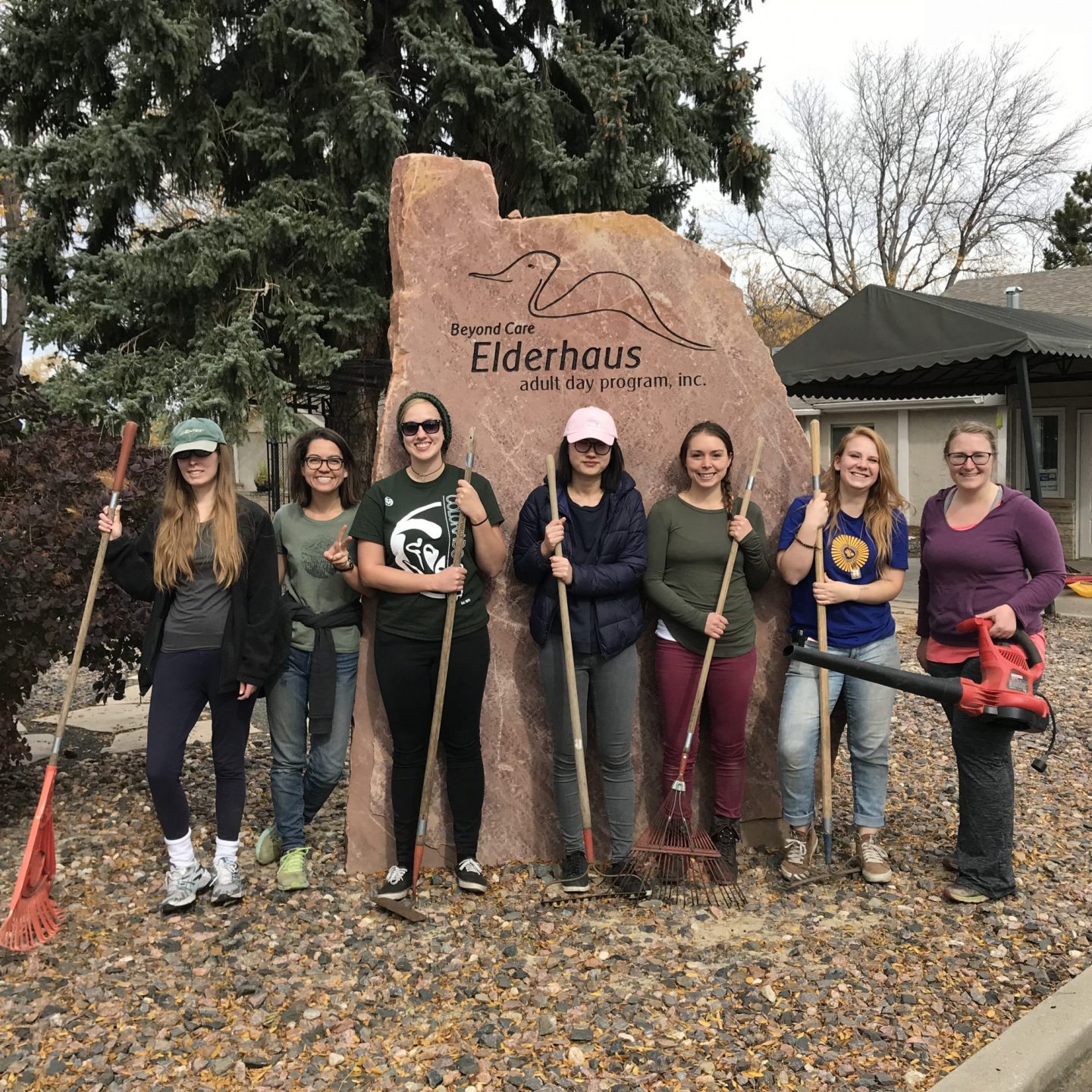 Student volunteers with rakes in front of a care facility