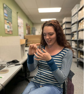 Student holding an artifact seated in chair in archaeological repository