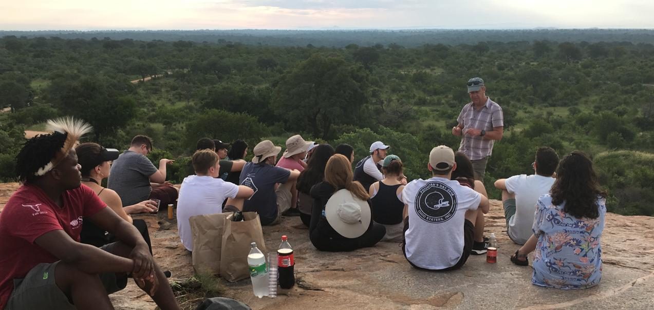 Professor speaking to a group on a cliff overlooking forest in national park in South Africa