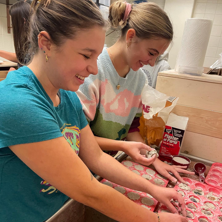 Two students packing sand and plaster mix into mini muffin molds making dig kits