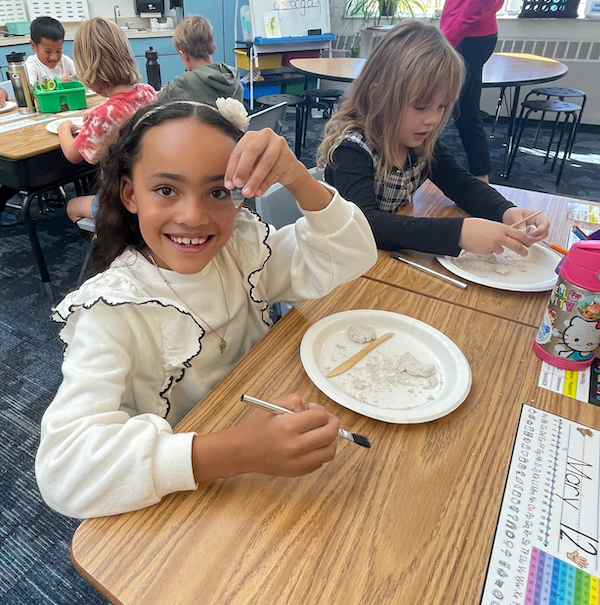 Elementary school student holds a replica projectile point in front of a plate of sand