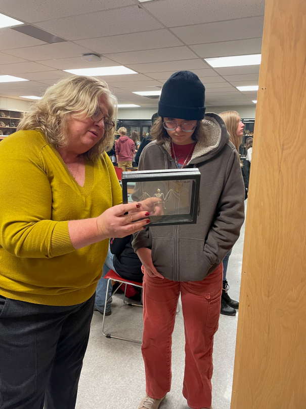 Female professor stands next to high school student looking at glass pressing of small primate skeleton