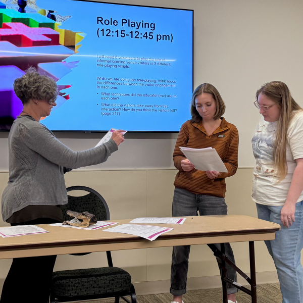Scientist standing next to graduate students as they share results of a public speaking exercise